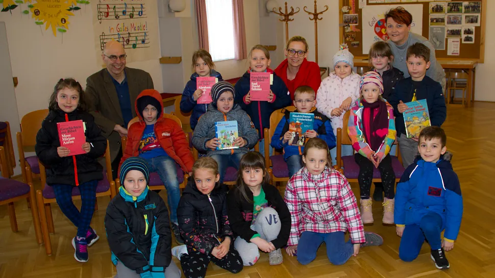 Eine Gruppe von Kindern und Erwachsenen, wahrscheinlich aus Kirche oder Schule, hält Bücher und lächelt.