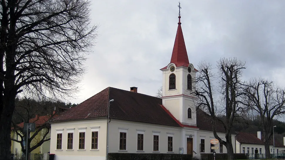 Weiße Kirche mit rotem Turm und braunem Dach, umgeben von kahlen Bäumen.