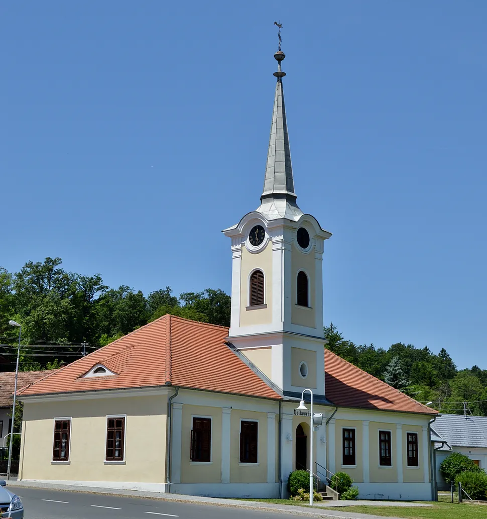 Cremefarbene Kirche mit rotem Ziegeldach und hohem Turm unter klarem blauem Himmel.