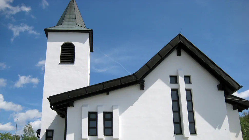 Moderne weiße Kirche mit dunklem Turm und kreuzförmigem Fenster.