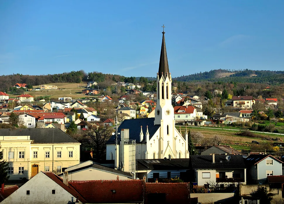 Eine hohe weiße Kirche mit dunklem Turm dominiert eine Bergstadt.