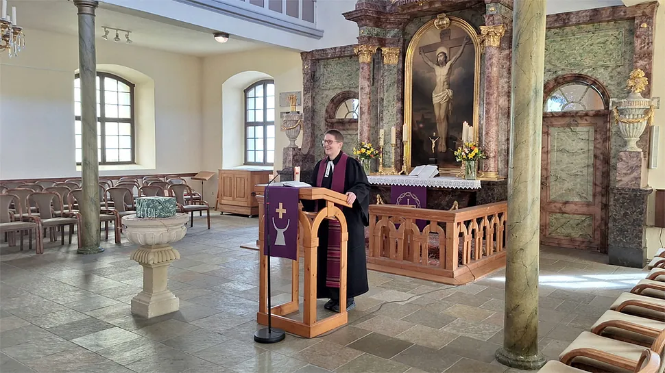 Ein Geistlicher predigt von einem Lesepult in einer Kirche mit verziertem Altar.