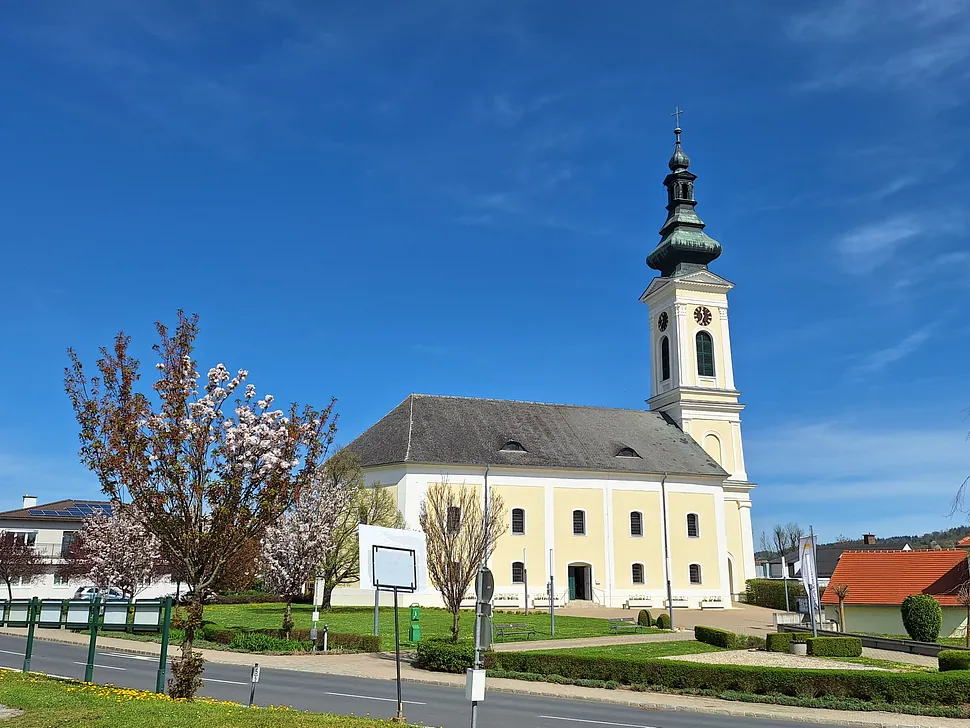 Historische gelbe Kirche mit grünem Kuppeldach und hohem Turm unter klarem blauem Himmel.