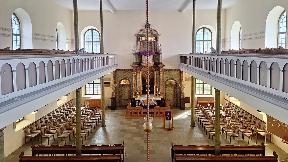 Kircheninneres von Empore, mit Bänken, verziertem Altar und hohen Fenstern.
