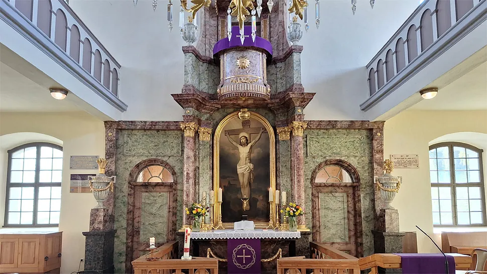 Aufwendiger Kirchenaltar mit großem Kruzifix, Kerzen und lila liturgischen Farben.