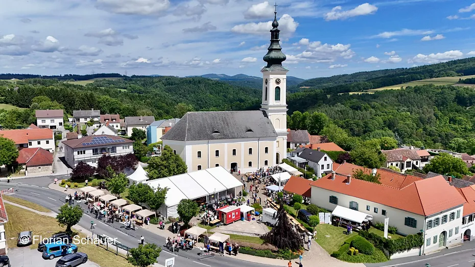 Luftaufnahme eines Stadtfestes um eine markante Kirche mit hohem Turm.