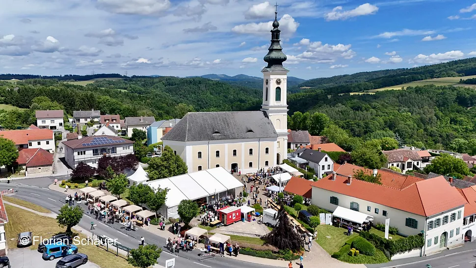 Luftaufnahme eines Stadtfestes um eine markante Kirche mit hohem Turm.
