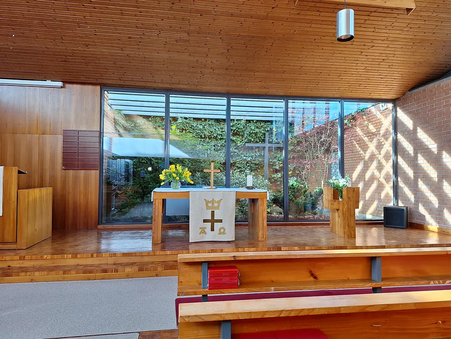 Moderner Kirchenaltar mit Kreuz und Banner, vor großen Fenstern mit Blick ins Grüne.