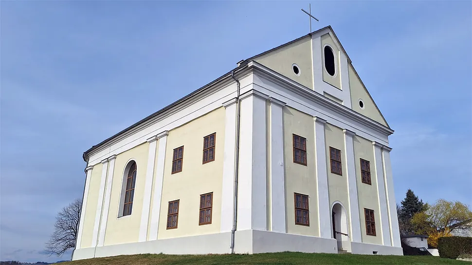 Historisches, schlichtes Kirchengebäude mit Kreuz, auf einem grasbewachsenen Hügel.