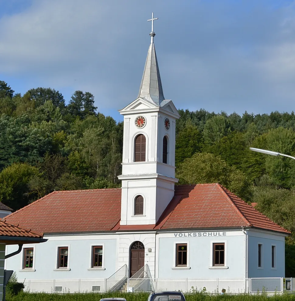 Cremefarbene Kirche mit rotem Ziegeldach und hohem Turm unter klarem blauem Himmel.