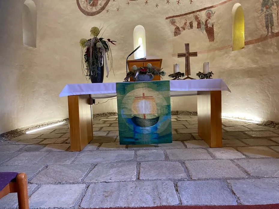 Kirchenaltar mit Kreuz, Kerzen und Banner, in rustikaler Umgebung.