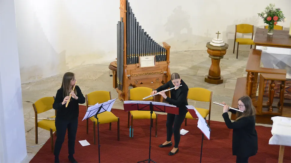Drei Musikerinnen spielen Flöten in einer Kirche, mit Orgel im Hintergrund.