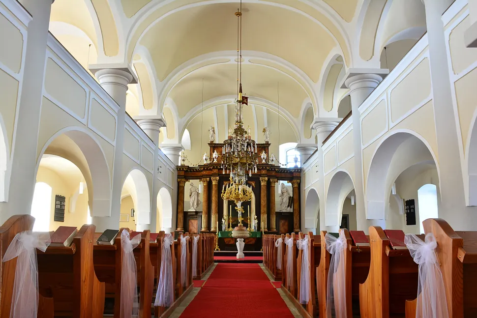 Kircheninneres mit rotem Teppich zum verzierten Altar, gesäumt von geschmückten Bänken.